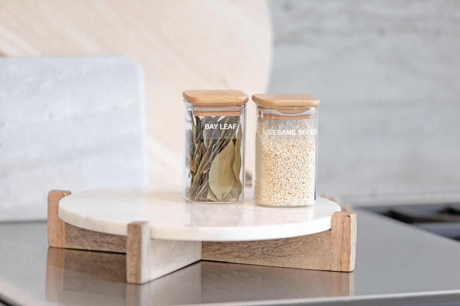 Spice Jars filled with bay leaf and sesame seeds placed on a tray on the countertop.