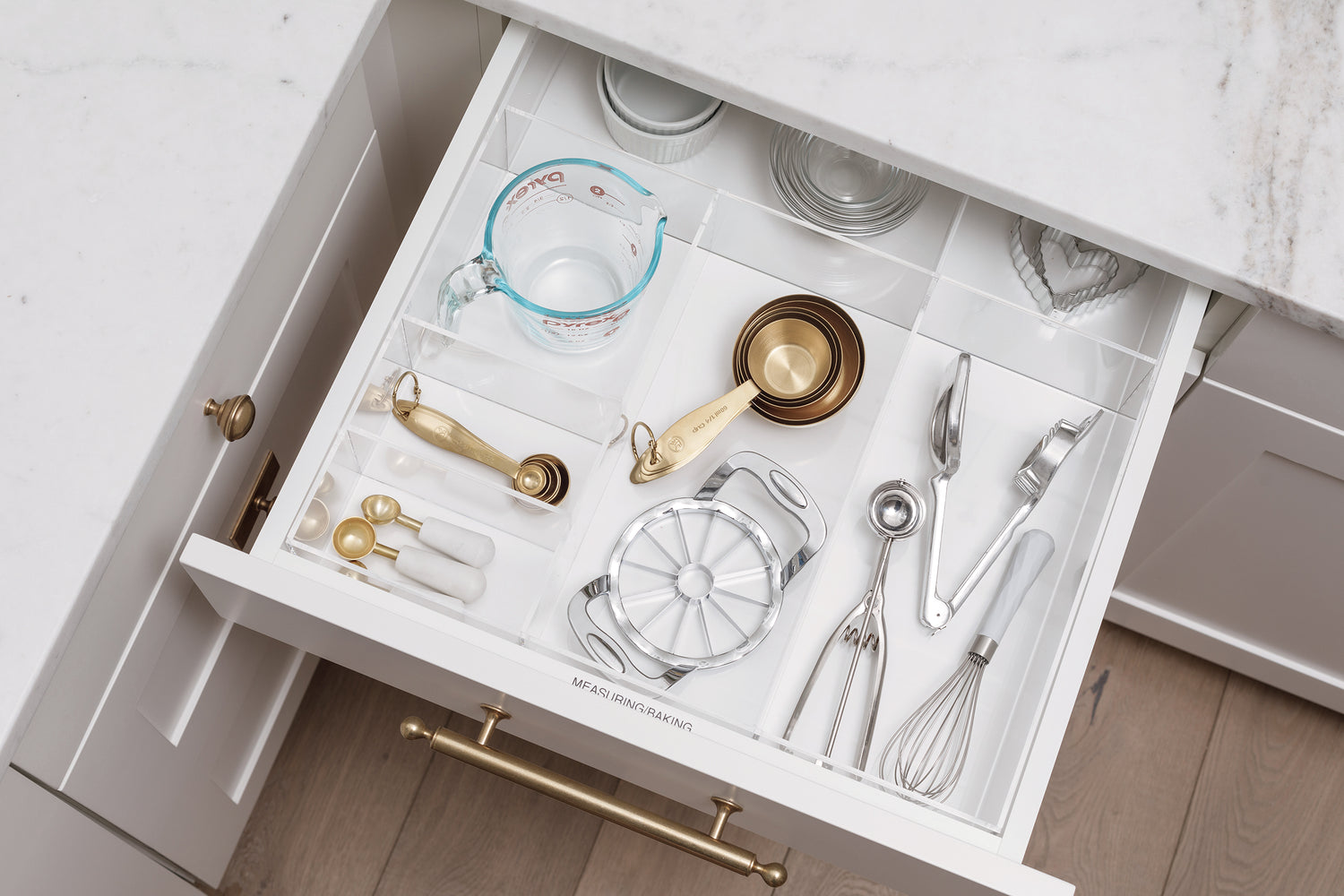 Measuring cups and spoons, along with other baking items well organized in an open kitchen drawer.