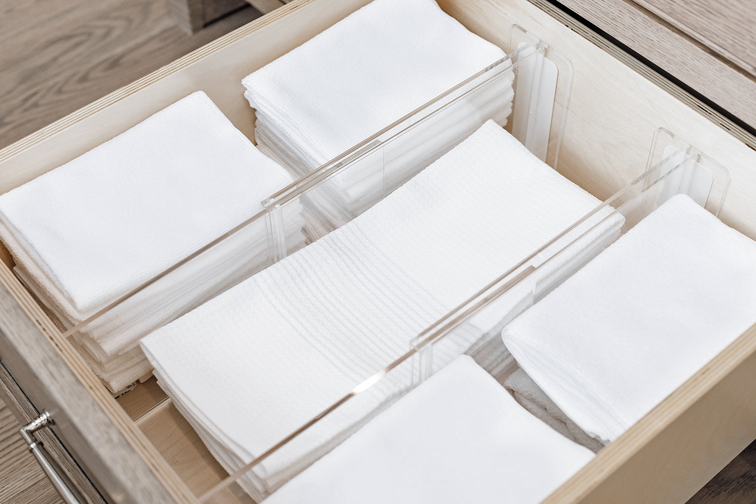 Three sections of white linens separated using Acrylic Drawer Dividers.
