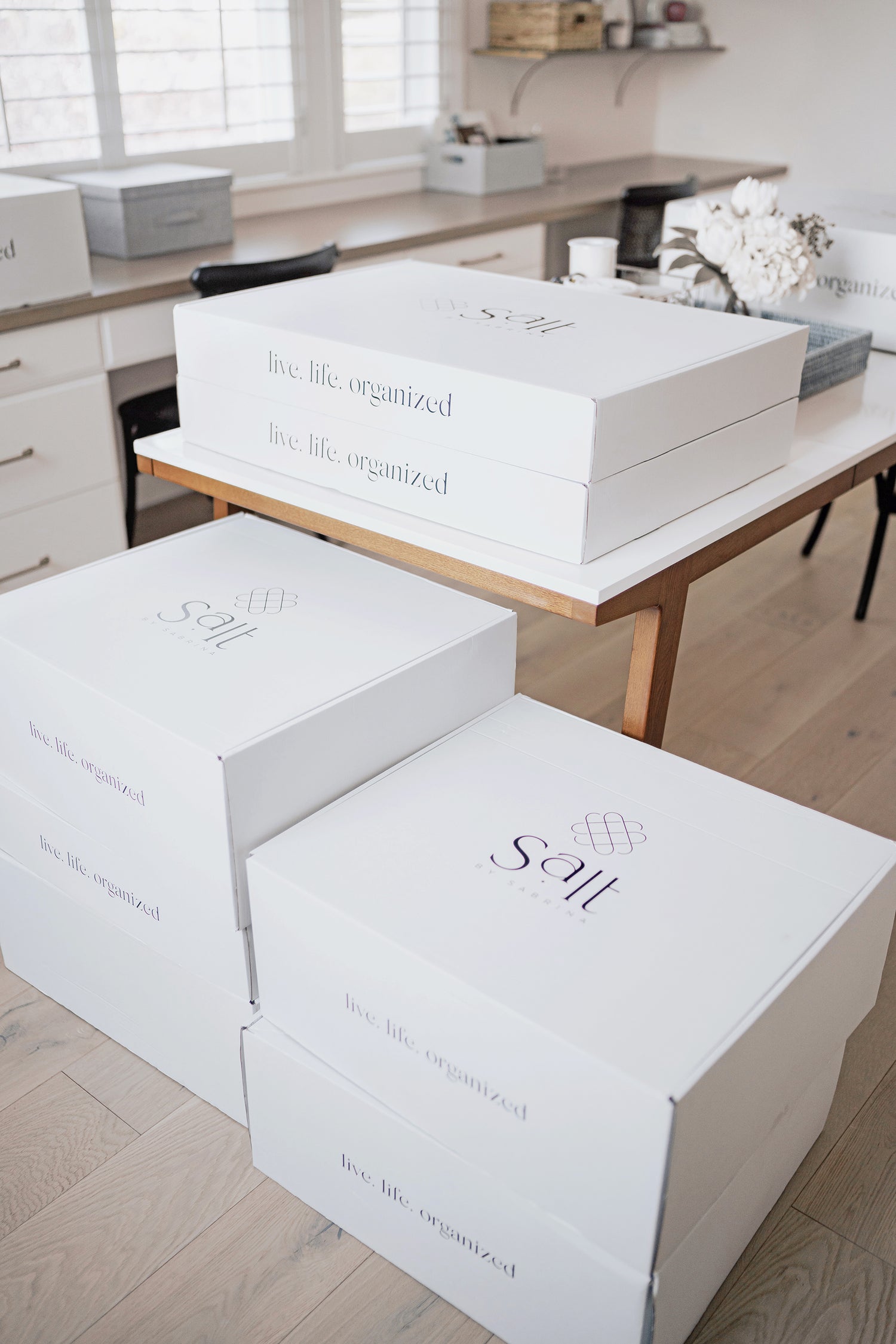 Tidy craft room with a stack of white Salt by Sabrina packages waiting to be opened.