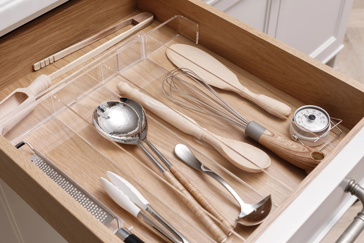 Crystal clear acrylic Expandable Kitchen Drawer Organizer separating wood and metal utensils.