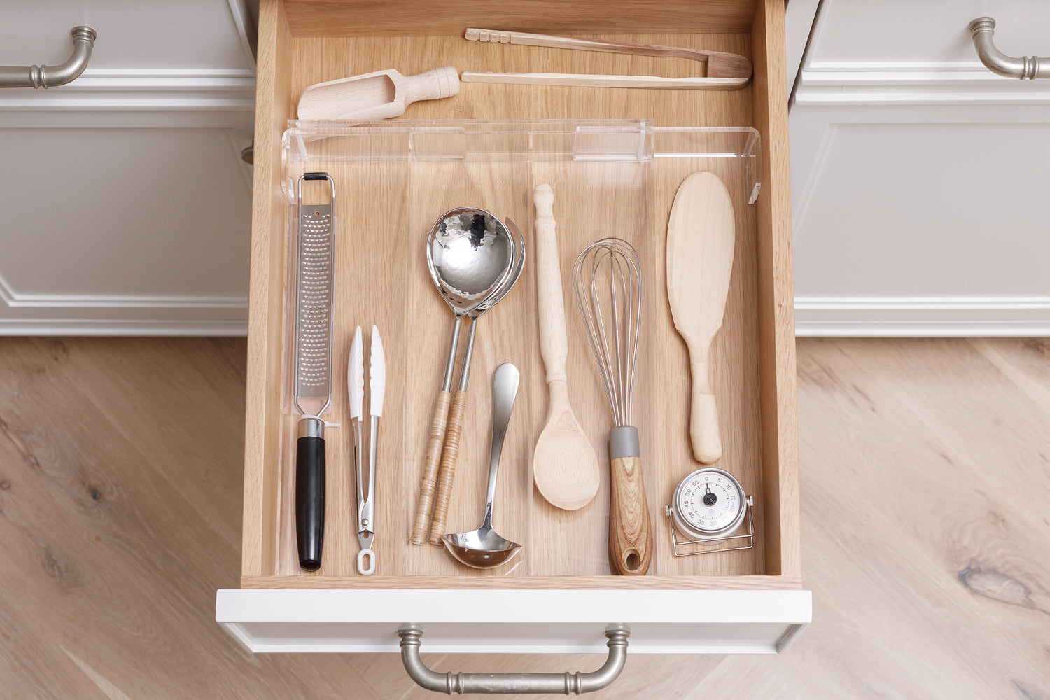Expandable acrylic organizer containing a variety of utensils in a kitchen drawer. 