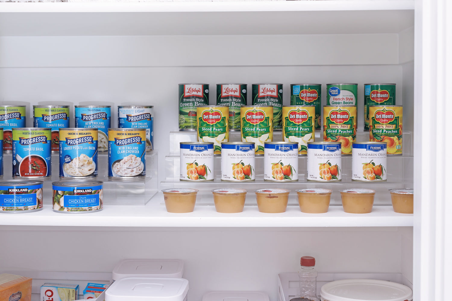 Canned goods stored in a cabinet on tiered acrylic spice racks. 