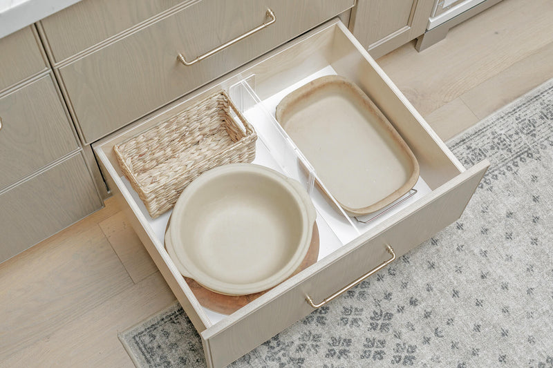 Acrylic drawer divider separating bakeware in an open kitchen drawer.