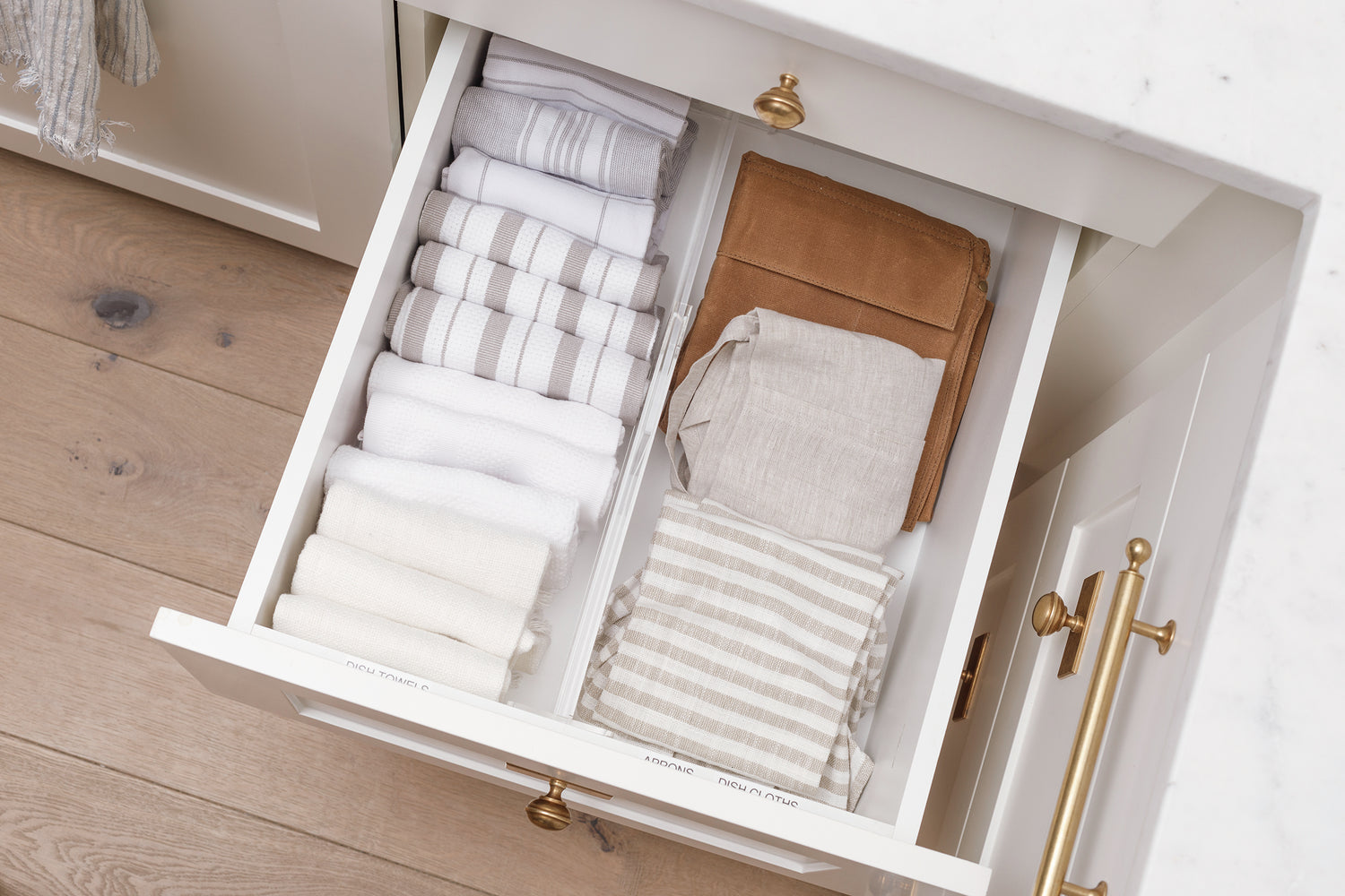 Linen drawer containing towels, aprons, and dishcloths separated by an Acrylic Drawer Divider.