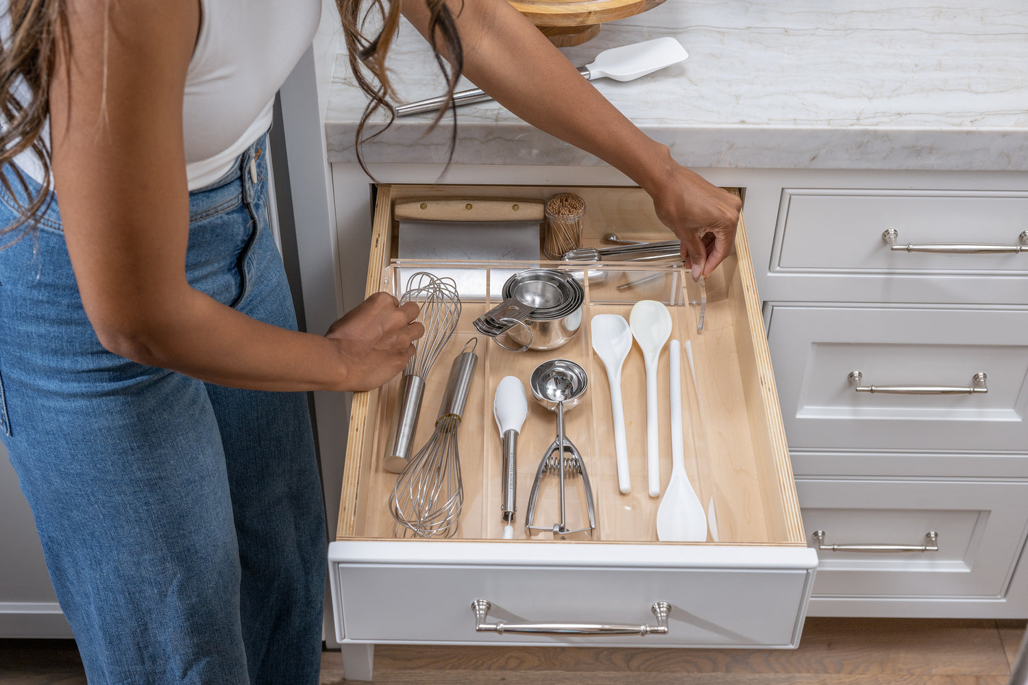 Woman adjusting an expandable drawer organizer to fit the size of her utensil drawer.