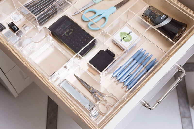 Close up view of a crystal clear acrylic drawer organizer in an office drawer holding essential products.