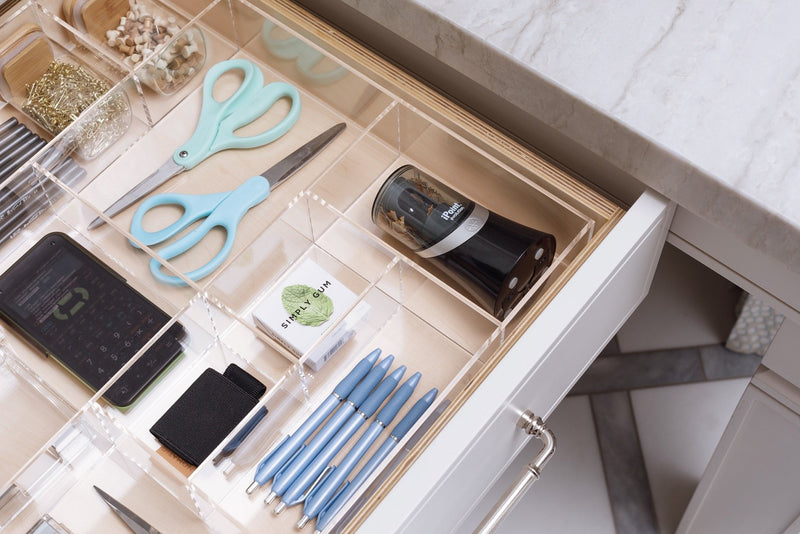 Close up view of a crystal clear acrylic drawer organizer in an office drawer holding essential products.