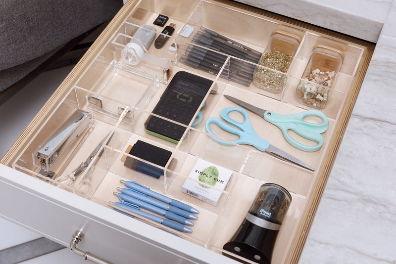 Crystal clear acrylic drawer organizer in an office drawer holding essential products.