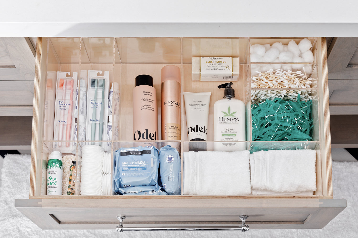 Bathroom drawer filled with supplies including toothbrushes, makeup wipes, and lotion, neatly organized with the Jennifer custom-fit organizer.