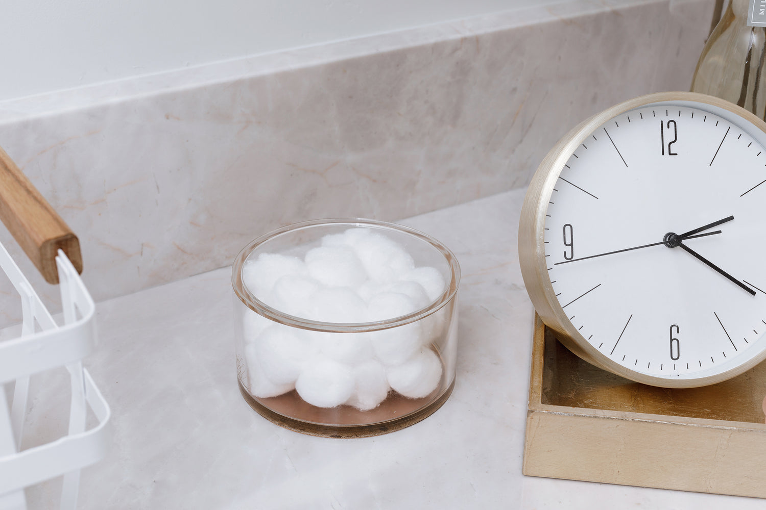 Cotton balls placed in a round acrylic storage container on the counter.