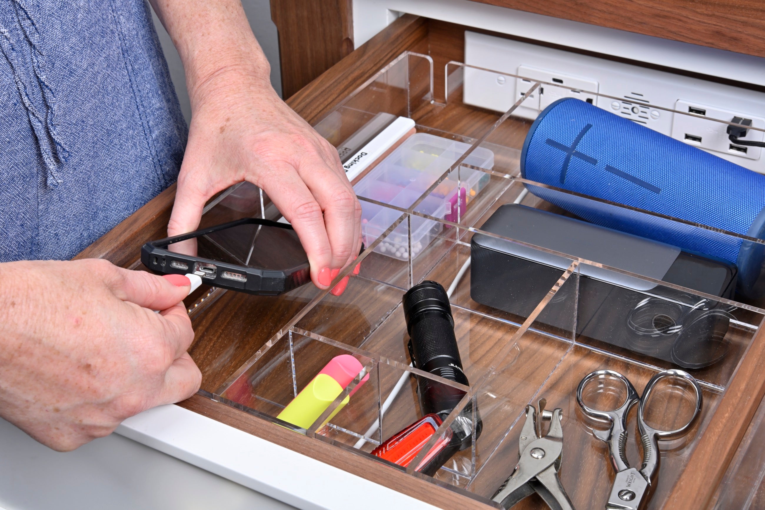 Woman plugs her in her phone to charge in her Docking Drawer with a custom-fit organizer. 