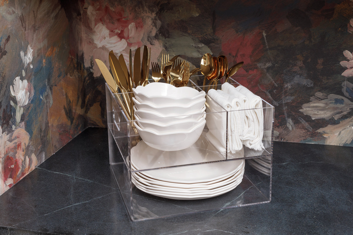Acrylic Utensil Caddy sitting on the counter fully stocked with gold cutlery, white dishes, and linen napkins.