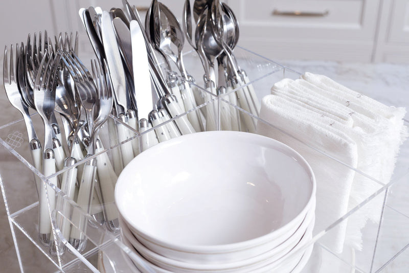 Close up view of the white bowls, silverware, and linen napkins stocked and ready to serve in the Acrylic Utensil Caddy.